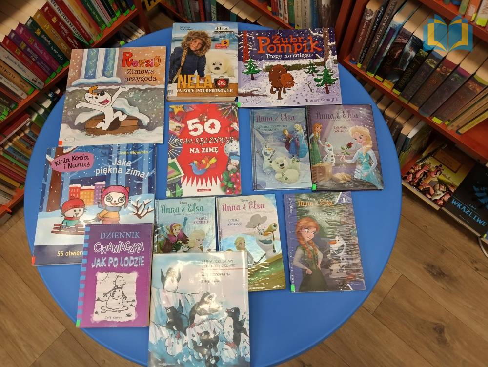 Zdjęcie: W bibliotece, na niebieskim stoliku, są ułożone książki dla dzieci o zimowej tematyce.